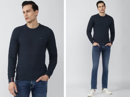 A person wearing a dark blue sweater, jeans, and white sneakers stands with hands partially in pockets.