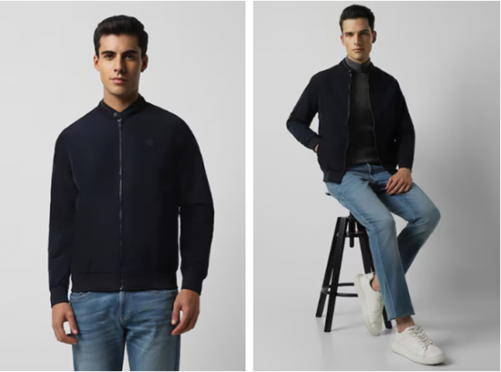 Man in a navy jacket and jeans standing and seated on a stool, modeling clothing.