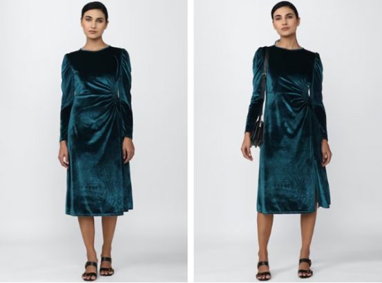 A person modeling a teal velvet dress with black accessories, posed against a white background.