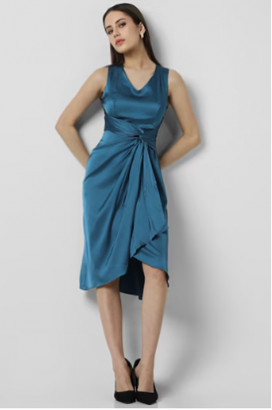 a woman standing in front of a wall wearing a blue dress